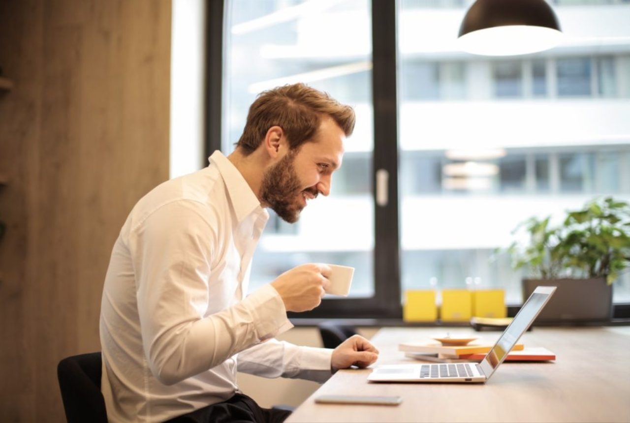 man-at-desk-holding-cup-of-coffee-looking-pleased-at notebook-coffee-cup-daytime-925786