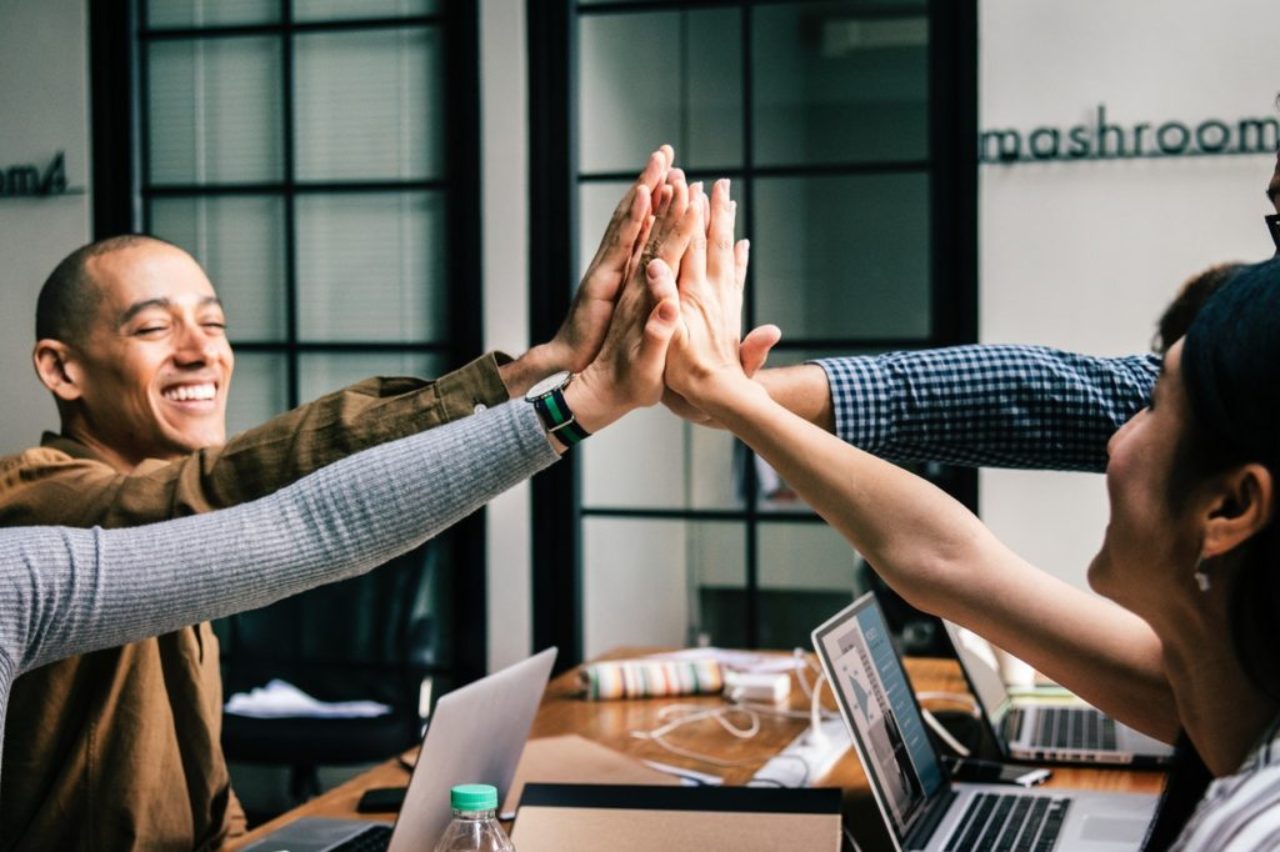 group-of-four-workers-at-theri-workstations-high-five-together