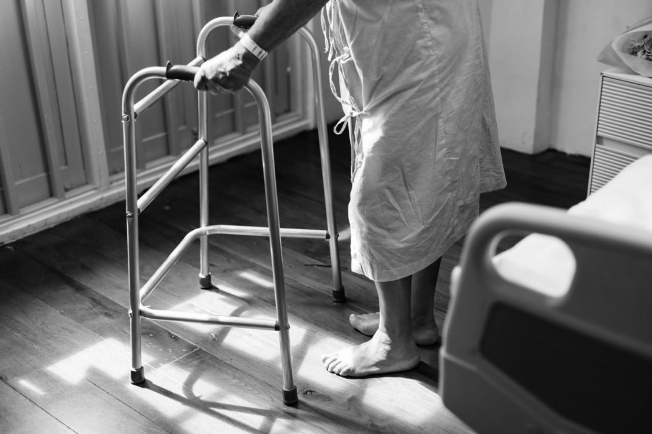 patient-in-gown-standing-next-to bed-holding-walker