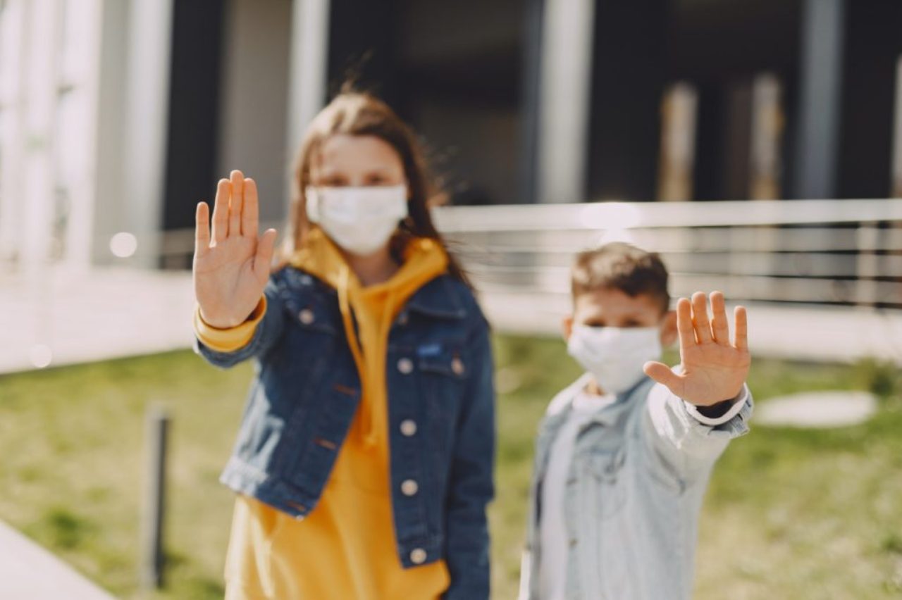 young-friends-with-medical-masks-on-street-hands-indicating-stop-4127435